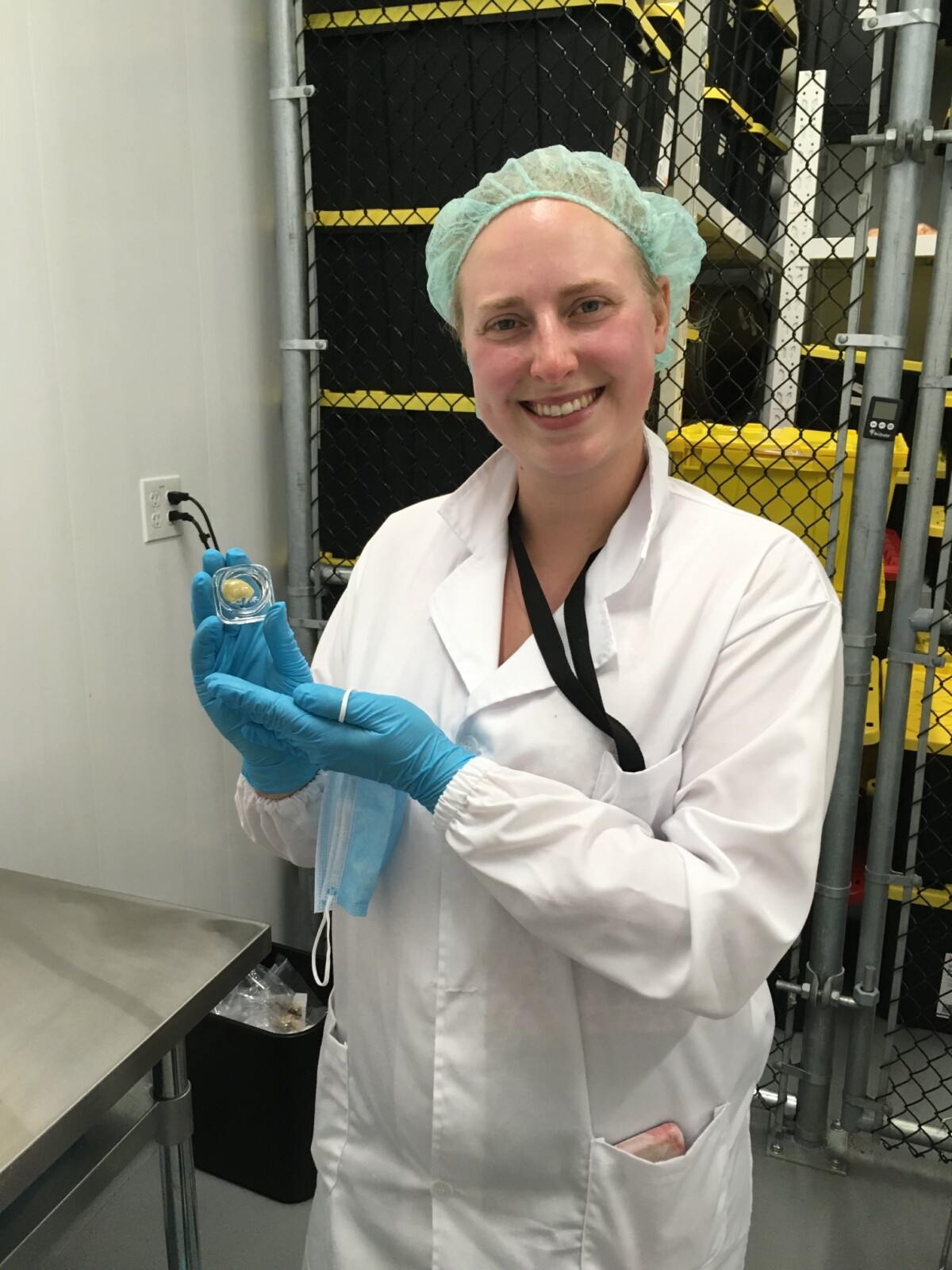 Alannah Davis, Chief Executive Officer & QAP of Dabble Cannabis Co., in a lab coat and hairnet, smiling as she holds up a glass container with cannabis concentrates.